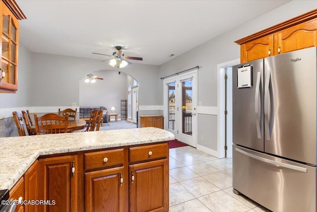 kitchen featuring arched walkways, french doors, brown cabinetry, and freestanding refrigerator