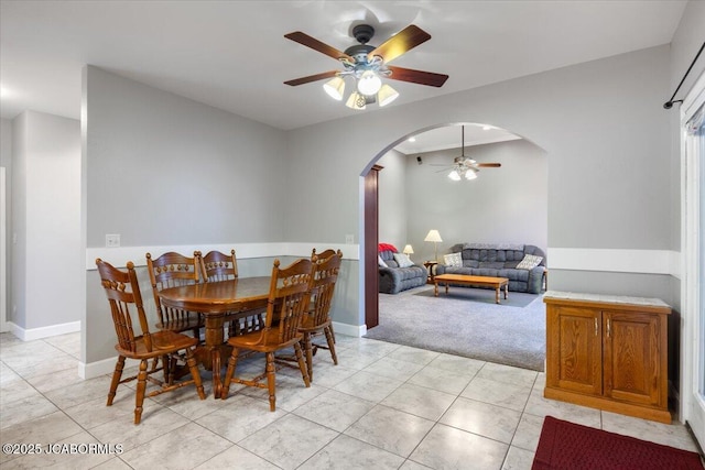 dining area featuring light carpet, baseboards, arched walkways, and a ceiling fan