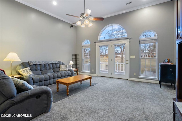 carpeted living room featuring visible vents, a towering ceiling, ornamental molding, a ceiling fan, and baseboards