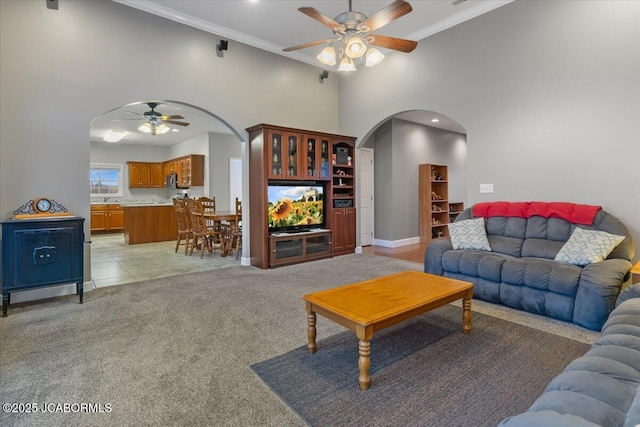 living room featuring light carpet, ceiling fan, arched walkways, and ornamental molding