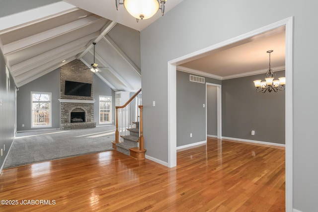 unfurnished living room with wood finished floors, visible vents, stairs, a brick fireplace, and ceiling fan with notable chandelier