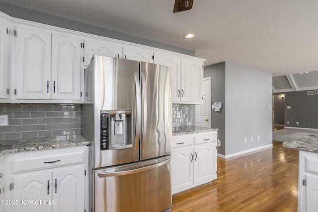 kitchen featuring light wood finished floors, baseboards, decorative backsplash, white cabinets, and stainless steel fridge