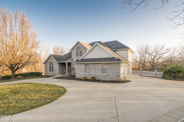 traditional-style home featuring curved driveway, fence, a front yard, a shingled roof, and brick siding