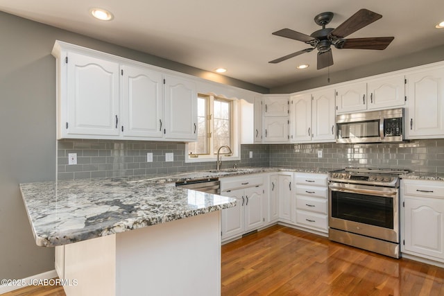 kitchen with a peninsula, light wood-style flooring, a sink, white cabinets, and appliances with stainless steel finishes