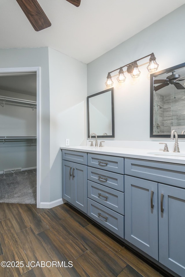 bathroom featuring wood finished floors, tiled shower, double vanity, a sink, and ceiling fan