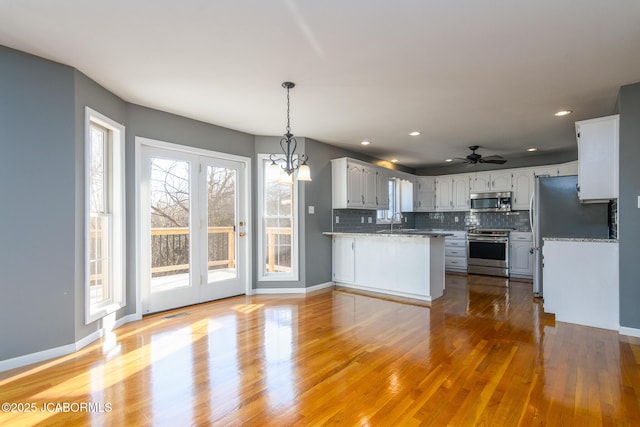 kitchen with tasteful backsplash, light wood-style flooring, appliances with stainless steel finishes, a peninsula, and a sink