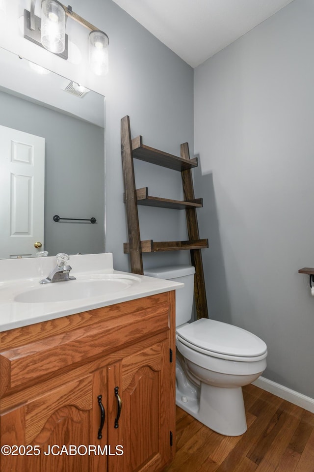 bathroom with visible vents, baseboards, toilet, wood finished floors, and vanity