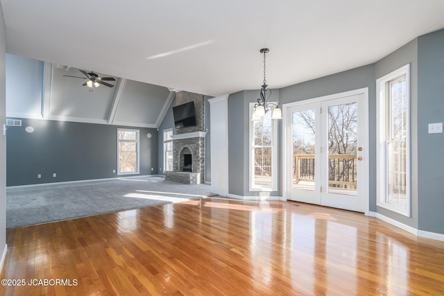 unfurnished living room with visible vents, ceiling fan with notable chandelier, wood finished floors, a large fireplace, and lofted ceiling