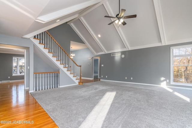 unfurnished living room with stairs, ceiling fan with notable chandelier, a wealth of natural light, and high vaulted ceiling