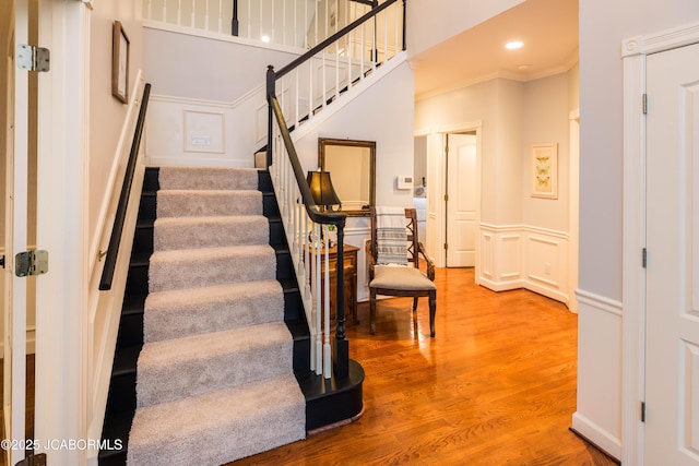 staircase with wood-type flooring and ornamental molding