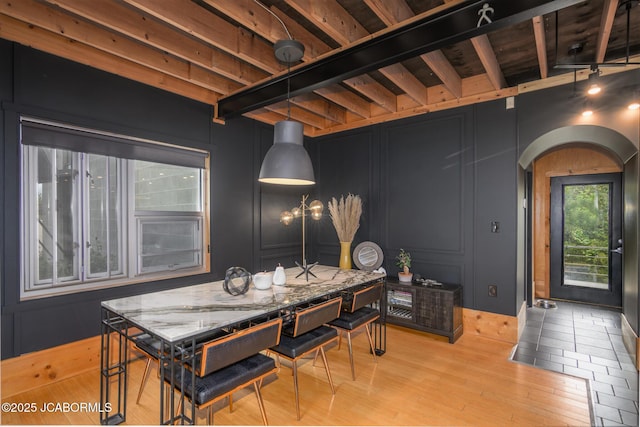 dining room featuring beam ceiling, arched walkways, light wood-style floors, and a decorative wall