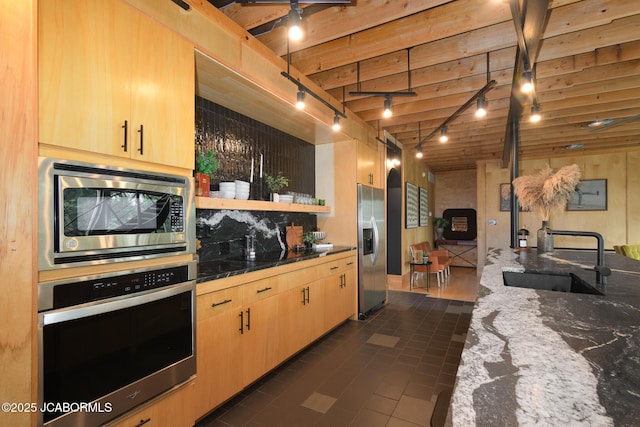 kitchen with a sink, stainless steel appliances, light brown cabinets, dark stone countertops, and rail lighting