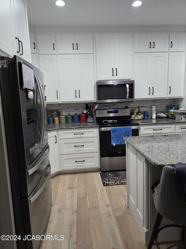 kitchen with appliances with stainless steel finishes, light hardwood / wood-style flooring, white cabinets, and tasteful backsplash