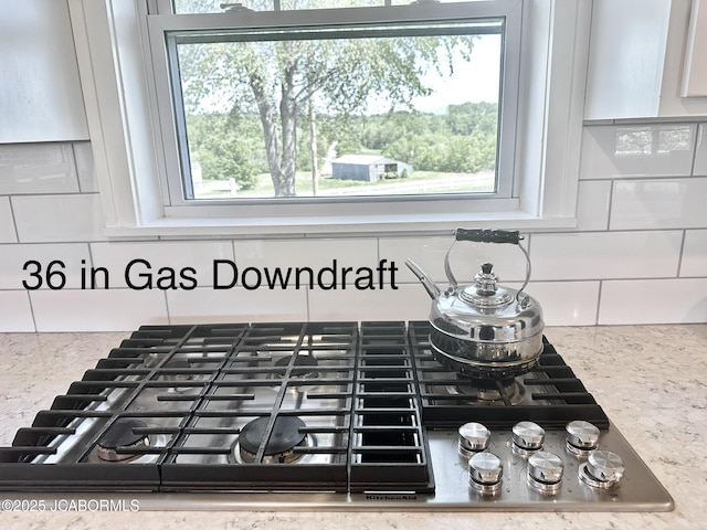 interior details with stainless steel gas cooktop, decorative backsplash, and light stone counters
