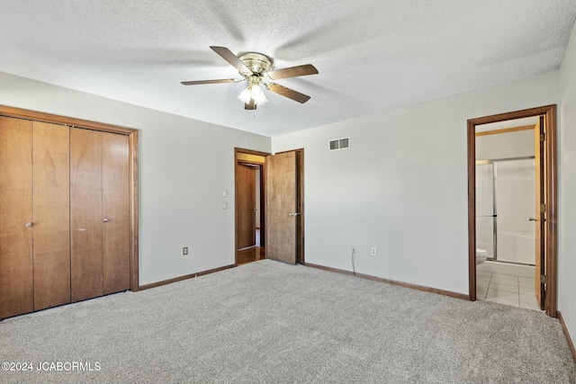 unfurnished bedroom with light carpet, a textured ceiling, ceiling fan, connected bathroom, and a closet