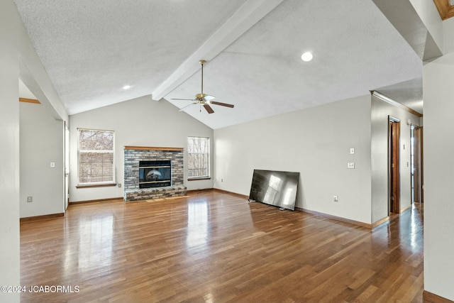 unfurnished living room with a textured ceiling, ceiling fan, hardwood / wood-style flooring, vaulted ceiling with beams, and a stone fireplace