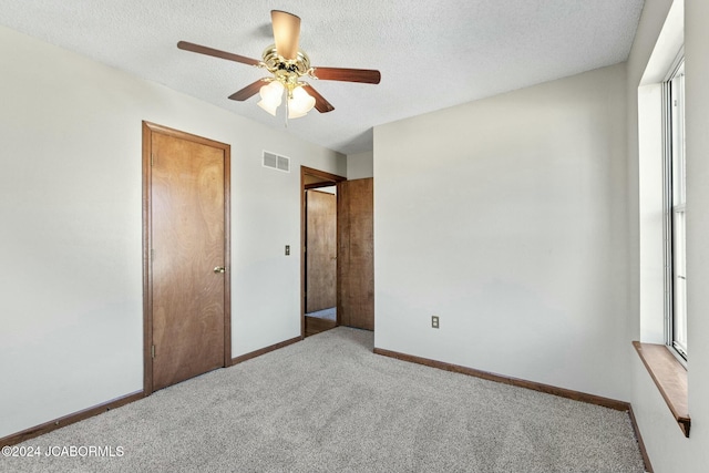 unfurnished bedroom with a textured ceiling, ceiling fan, light carpet, and multiple windows