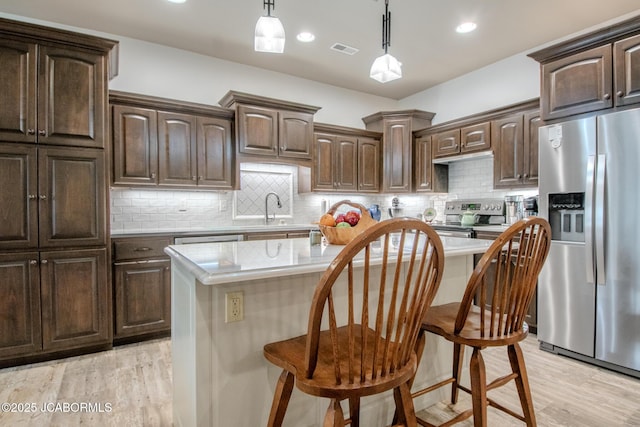 kitchen featuring a kitchen bar, hanging light fixtures, a center island, stainless steel appliances, and dark brown cabinets