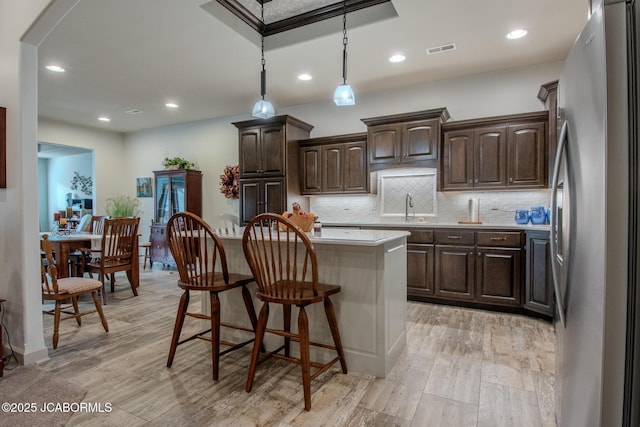 kitchen featuring a breakfast bar, sink, a center island, dark brown cabinets, and stainless steel fridge