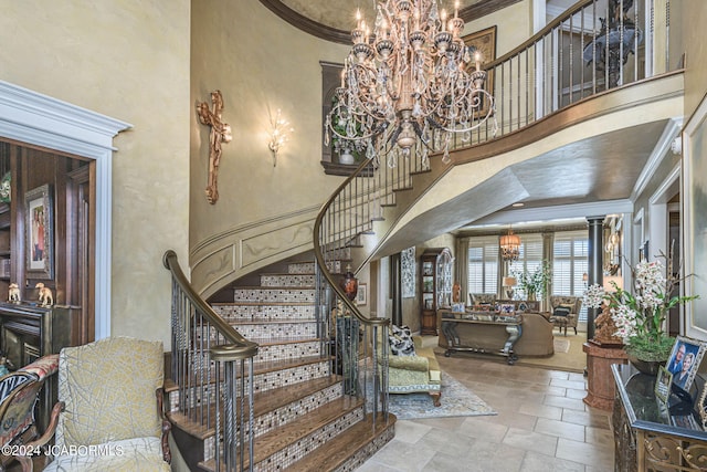 stairs with ornamental molding, a high ceiling, and an inviting chandelier