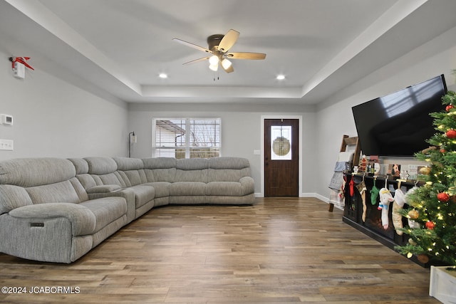 living room with wood-type flooring, a raised ceiling, and ceiling fan