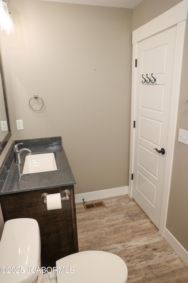 half bath with vanity, baseboards, wood finished floors, and toilet