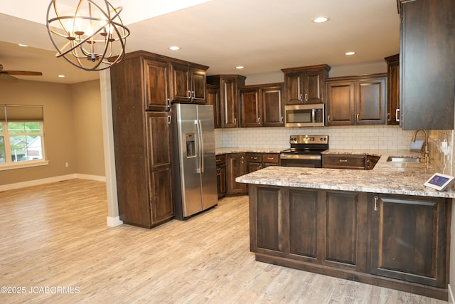 kitchen with dark brown cabinetry, appliances with stainless steel finishes, tasteful backsplash, light stone countertops, and a sink