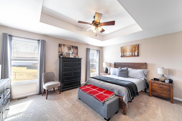 bedroom with visible vents, baseboards, light colored carpet, a raised ceiling, and a ceiling fan