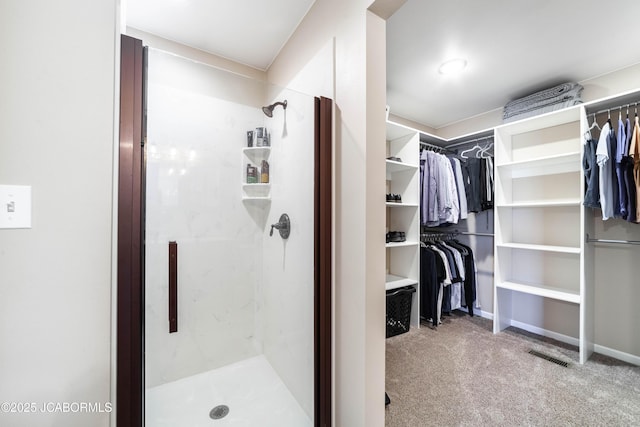 full bath featuring visible vents, a shower stall, a walk in closet, and baseboards