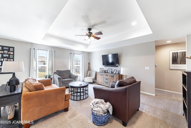 living room with a raised ceiling, a ceiling fan, recessed lighting, carpet flooring, and baseboards