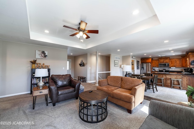 living area featuring a ceiling fan, baseboards, a tray ceiling, recessed lighting, and light colored carpet