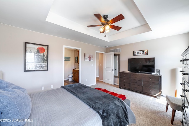 carpeted bedroom featuring visible vents, connected bathroom, baseboards, and a tray ceiling