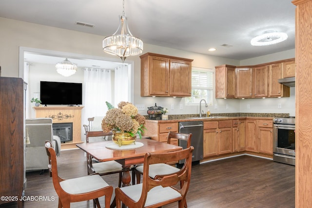 180 Venus St, Holts Summit, MO 65043 - kitchen with appliances with stainless steel finishes, a sink, under cabinet range hood, dark wood finished floors, and a glass covered fireplace