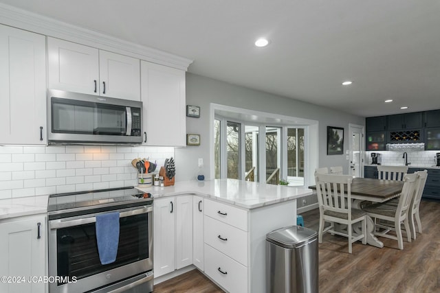 kitchen featuring kitchen peninsula, decorative backsplash, white cabinets, and appliances with stainless steel finishes