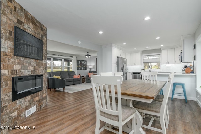 dining space featuring wood-type flooring, a stone fireplace, and a wealth of natural light