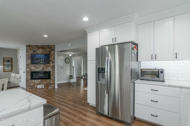 kitchen with dark wood-type flooring, stainless steel fridge, light stone countertops, a fireplace, and white cabinetry