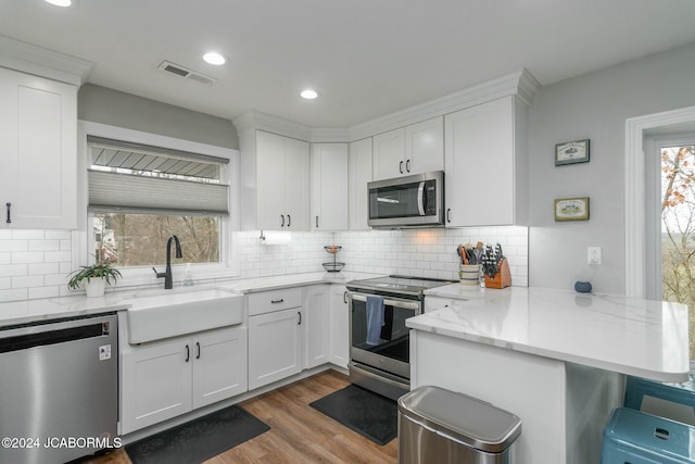 kitchen with kitchen peninsula, tasteful backsplash, stainless steel appliances, sink, and white cabinets