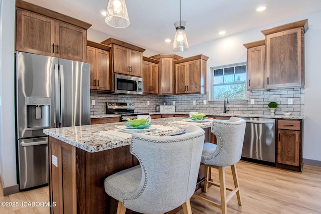 kitchen with appliances with stainless steel finishes, decorative light fixtures, a breakfast bar area, a center island, and light hardwood / wood-style flooring