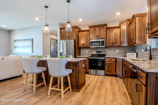 kitchen featuring sink, tasteful backsplash, light wood-type flooring, appliances with stainless steel finishes, and pendant lighting