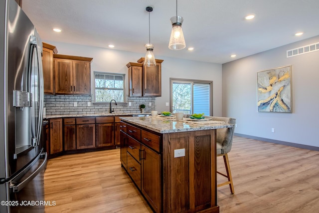 kitchen featuring a kitchen island, pendant lighting, a breakfast bar area, light stone counters, and stainless steel fridge with ice dispenser