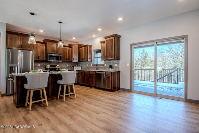 kitchen featuring appliances with stainless steel finishes, a center island, decorative backsplash, a kitchen bar, and decorative light fixtures