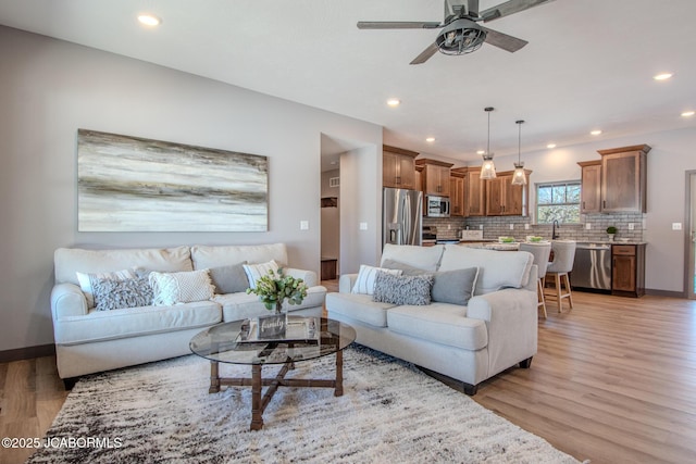 living room featuring sink, ceiling fan, and light wood-type flooring