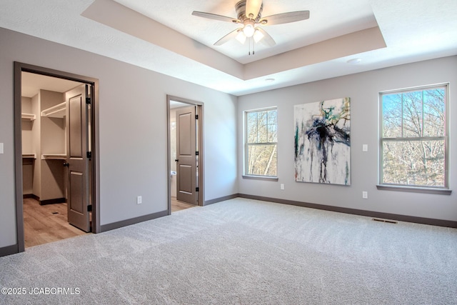 unfurnished bedroom featuring a spacious closet, light carpet, and a tray ceiling