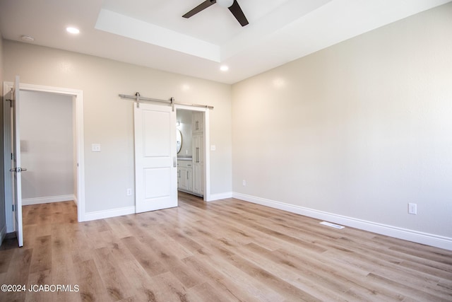 unfurnished bedroom with a barn door, baseboards, a raised ceiling, and light wood-type flooring