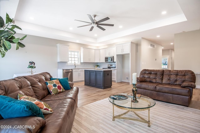 living room featuring a tray ceiling, light hardwood / wood-style flooring, ceiling fan, and sink