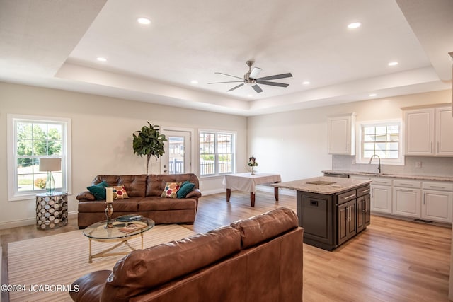 living room featuring light wood-type flooring, a tray ceiling, ceiling fan, and sink