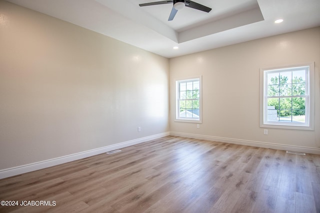 unfurnished room featuring a tray ceiling, ceiling fan, and light wood-type flooring