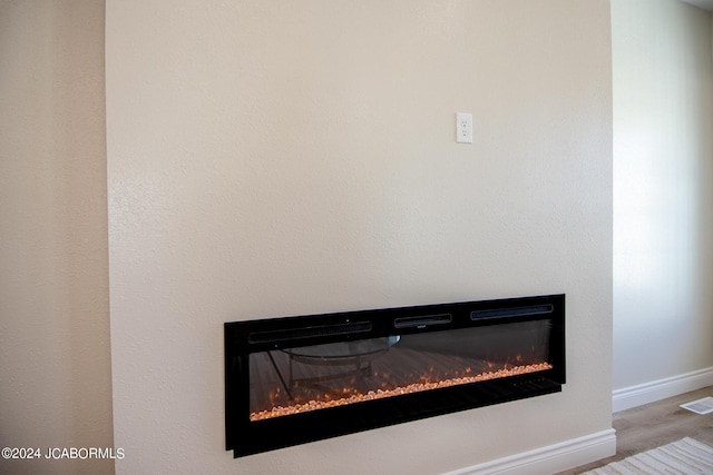 room details featuring a glass covered fireplace, wood finished floors, visible vents, and baseboards