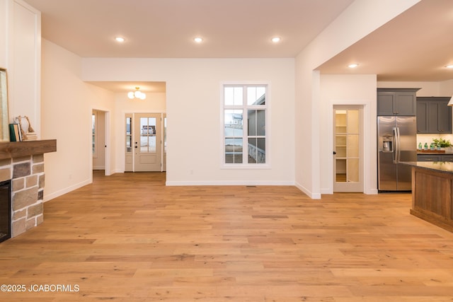 living area with recessed lighting, light wood-style flooring, baseboards, and a stone fireplace