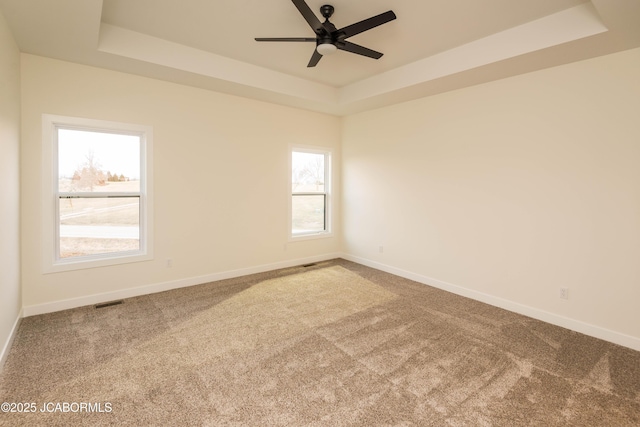 unfurnished room with carpet, a tray ceiling, baseboards, and ceiling fan